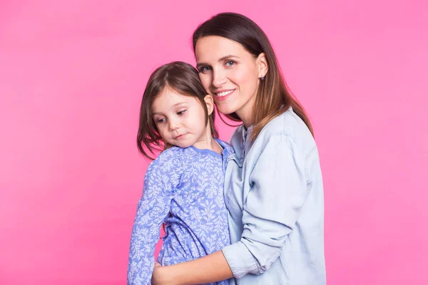 Pessoas, felicidade, amor, família e maternidade conceito - pequena filha feliz abraçando e beijando sua mãe sobre fundo rosa — Fotografia de Stock