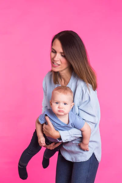 Feliz jovem mãe com um bebê criança no fundo rosa — Fotografia de Stock
