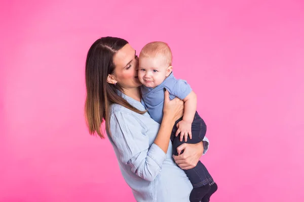 Feliz jovem mãe com um bebê criança no fundo rosa — Fotografia de Stock