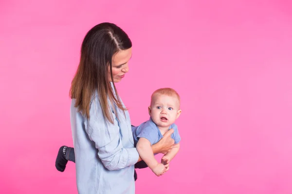 Familia, maternidad, crianza, personas y concepto de cuidado infantil - madre feliz sostiene adorable bebé sobre fondo rosa — Foto de Stock