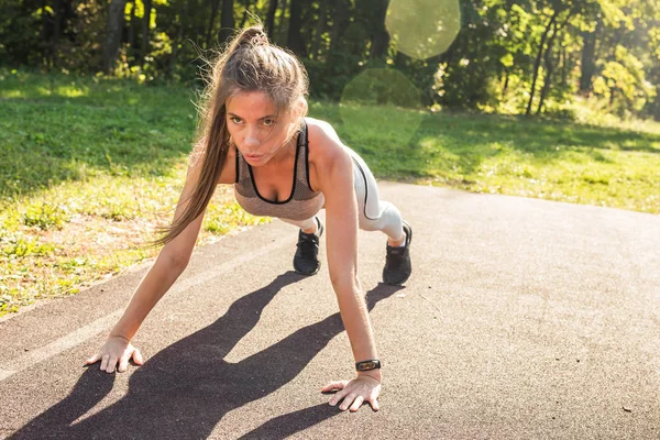 Femme de remise en forme faisant push-ups pendant l'entraînement cross extérieur. Belle jeune et forme physique sport modèle entraînement à l'extérieur dans le parc — Photo