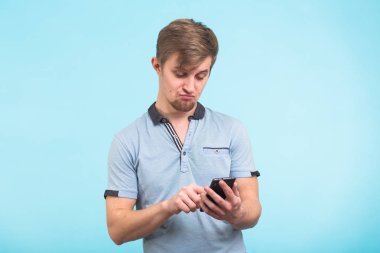 Komik adam akıllı telefon üzerinde mavi arka plan izole manifatura iletide. Akıllı telefon tutarak ve bakarak gülen adam.