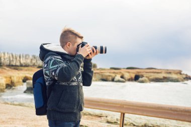 Deniz ve kayalar fotoğraflarını fotoğraf makinesi ile yapım sırt çantası ile genç fotoğrafçı. Akdeniz