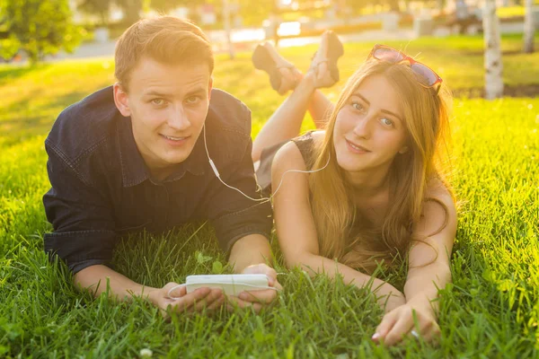 Jovem casal adorável ou estudantes universitários deitados na grama juntos, ouvindo música . — Fotografia de Stock