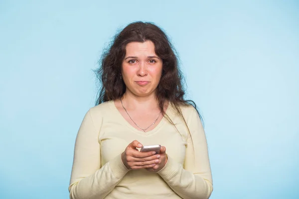 Mujer infeliz resentida sosteniendo el teléfono inteligente mirando la cámara sobre fondo azul — Foto de Stock