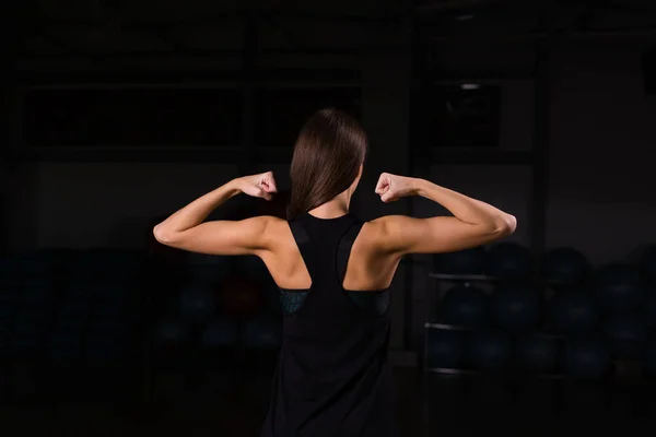 背中の筋肉と手を孤立した黒の背景に示す陸上競技の若い女性 — ストック写真