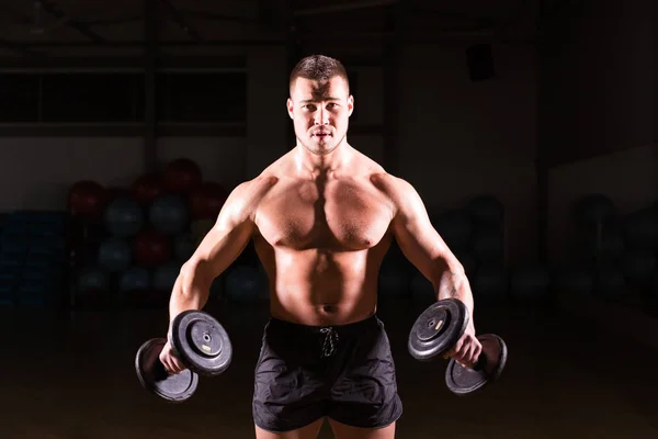 М'язистий молодий чоловік піднімає ваги на темному тлі — стокове фото