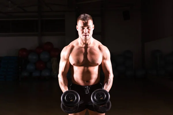 Kraftvoller Bodybuilder, der die Übungen mit Kurzhanteln macht. kräftiges Männchen mit nacktem Oberkörper auf dunklem Hintergrund. Stärke und Motivation. — Stockfoto
