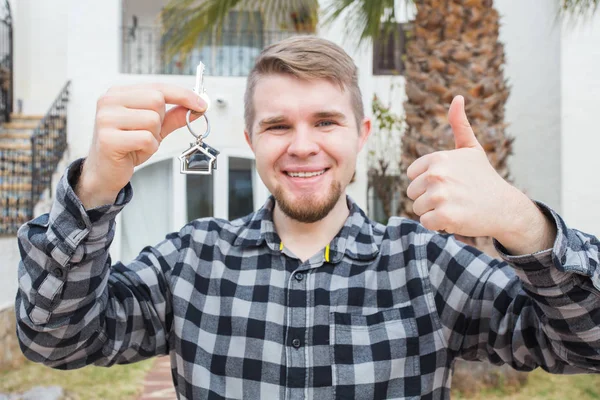 Young happy man showing a house key and thumbs up. — Stock Photo, Image