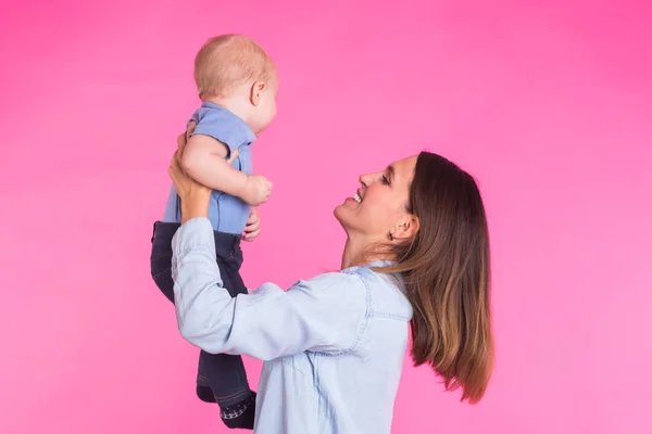 Familia, maternidad, crianza, personas y concepto de cuidado infantil - madre feliz sostiene adorable bebé sobre fondo rosa — Foto de Stock