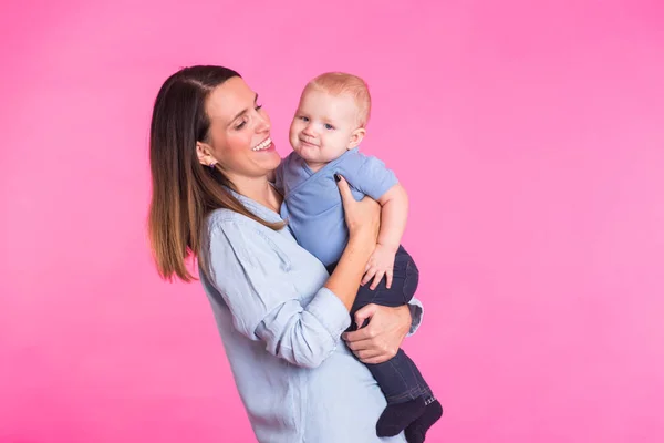 Familia, maternidad, crianza, personas y concepto de cuidado infantil - madre feliz sostiene adorable bebé sobre fondo rosa — Foto de Stock