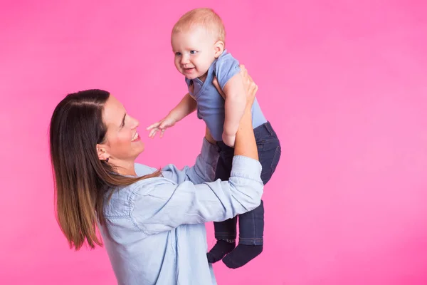 Familia, maternidad, crianza, personas y concepto de cuidado infantil - madre feliz sostiene adorable bebé sobre fondo rosa — Foto de Stock