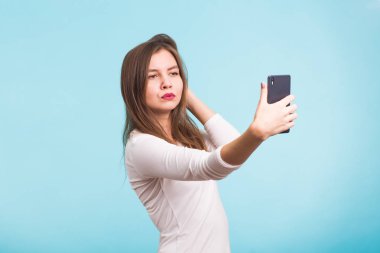Neşeli genç kadın selfie akıllı telefonunu mavi arka plan yapma