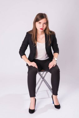 Tam uzunlukta stüdyo portre siyah takım, yüksek topuk ayakkabı, beyaz arka plan üzerinde sandalyede oturan genç iş kadını