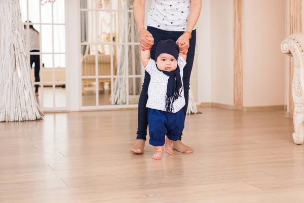 Мать держит малыша за руки, чтобы помочь ему ходить. Первый шаг концепции — стоковое фото