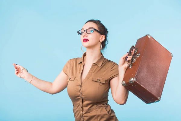 Porträt einer aufgeregten jungen Frau mit einem Koffer vor blauem Hintergrund, Reisen, Urlaub und Urlaubskonzept. — Stockfoto