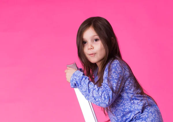 Glad liten tjej på en hopfällbar stege över rosa bakgrund — Stockfoto