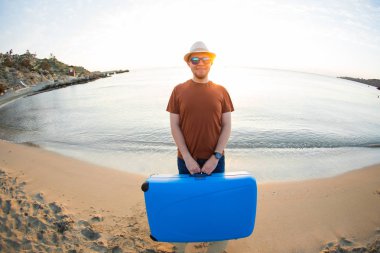 Bavul tutarak ve gösterilen adam mavi okyanusun karşı başparmak. Seyahat kavramı.