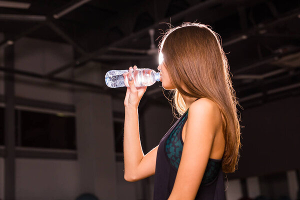 Fitness young woman drinking water in the gym. Muscular woman taking break after exercise