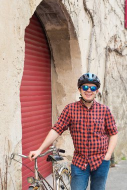 Genç gülümseyen adam, kask, Bisiklet üzerinde açık kırmızı gömlek ve güneş gözlüğü tutun