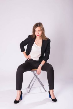 Tam uzunlukta stüdyo portre siyah takım, yüksek topuk ayakkabı, beyaz arka plan üzerinde sandalyede oturan genç iş kadını