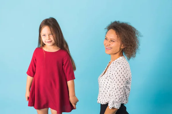 Feliz madre e hija abrazando y sonriendo a la cámara aislada en azul — Foto de Stock