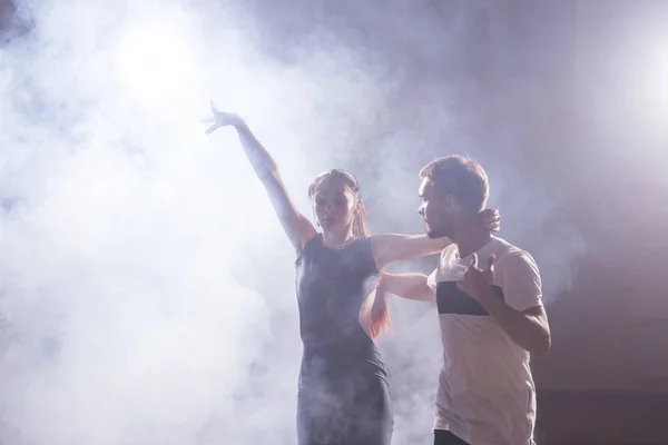 Bailarines hábiles actuando en la sala oscura bajo la luz del concierto y el humo. Pareja sensual realizando una danza contemporánea artística y emocional — Foto de Stock