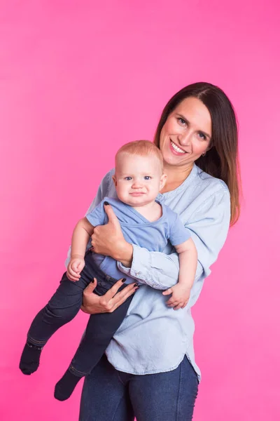 Familia, maternidad, crianza, personas y concepto de cuidado infantil - madre feliz sostiene adorable bebé sobre fondo rosa — Foto de Stock