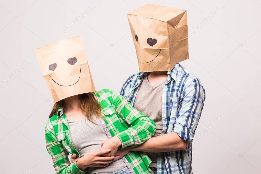 Love couple covering their faces with paper bag over white background