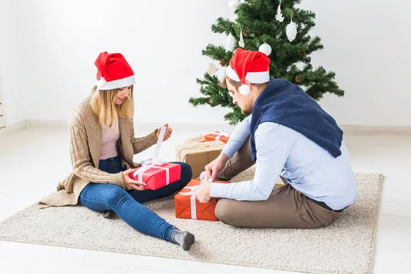 Koncepcja świąteczna - słodka para otwierająca prezenty świąteczne, siedząca w salonie — Zdjęcie stockowe