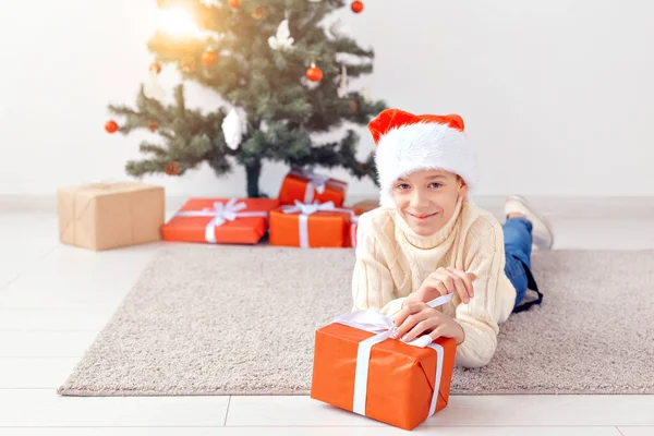 크리스마스, 크리스마스, 아동기, 사람들의 컨셉 - 크리스마스 트리 배경 위에 선물 상자가 놓인 산타 모자를 쓴 행복 한 10 대 소년웃는 모습 — 스톡 사진