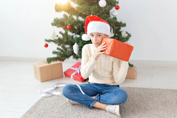 크리스마스, 크리스마스, 아동기, 사람들의 컨셉 - 산타 모자를 쓴 행복 한 10 대 소년 이 크리스마스 트리 배경 위에 선물 상자를 열다. — 스톡 사진