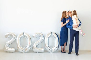 Genç, mutlu aile babası ve kızı beyaz arka planda 2020 numaralı balonların yanında duruyorlar. Yeni yıl, Noel, tatil