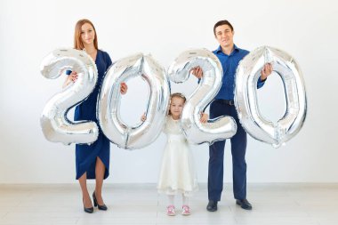 Genç mutlu aile babası, anne ve kızı ellerinde 2020 numara şeklinde balonlar tutuyorlar beyaz arka planda. Yeni yıl, Noel, tatil