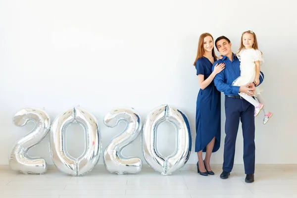 Joven familia feliz madre y padre e hija de pie cerca de globos en forma de números 2020 sobre fondo blanco. Año nuevo, Navidad, vacaciones — Foto de Stock