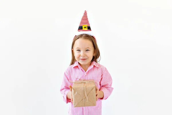Bambino divertente sorridente in cappello rosso Santa tenendo in mano la scatola regalo su sfondo bianco con copyspace. Concetto Natale . — Foto Stock