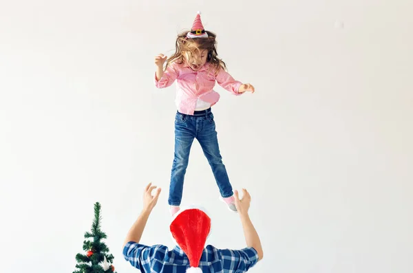 Navidad, vacaciones y el concepto de paternidad - papá divertido con sombrero de santa arroja a su hija sobre fondo blanco con espacio para copiar — Foto de Stock
