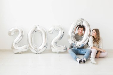 Tatiller, şenlik ve parti konsepti. Beyaz arka planda, gümüş 2020 balon yakınında oturan komik bir çift. Yeni yıl kutlaması
