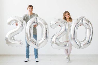 Tatiller, şenlik ve parti konsepti mutlu çift, beyaz arka planda gümüş 2020 balon tutuyor. Yeni yıl kutlaması