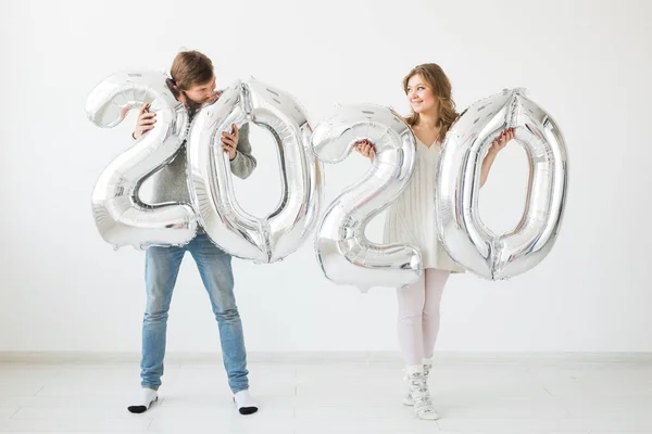 Vacaciones, fiesta y concepto de fiesta - Feliz pareja amorosa sostiene globos de plata 2020 sobre fondo blanco. Celebración de Año Nuevo — Foto de Stock