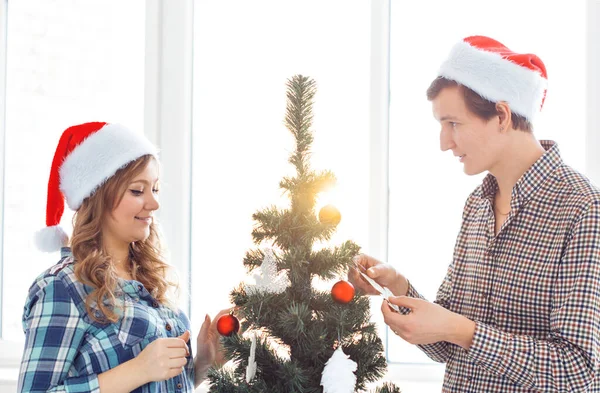 Család, x-mas, téli ünnepek és emberek koncepció - boldog fiatal pár díszítő karácsonyfa otthon — Stock Fotó