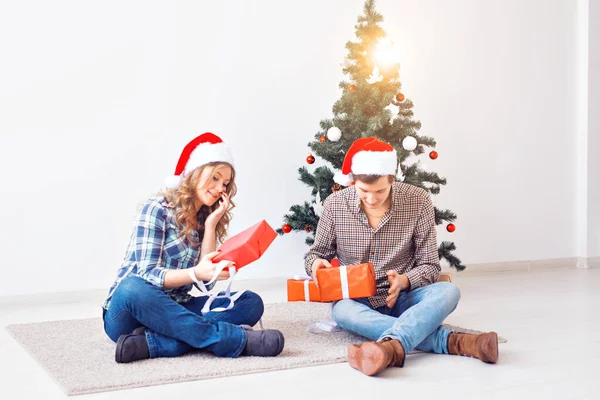 Święta, Boże Narodzenie i koncepcja rodziny - Młoda szczęśliwa para otwiera prezenty w domu. — Zdjęcie stockowe