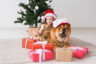 Çocuklar ve evcil hayvan konsepti. Noel ağacının yanında oturan köpekli tatlı kız. Mutlu Noeller ve mutlu tatiller.