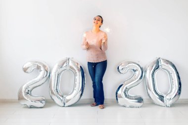 New Year celebration and party concept - Happy young woman with sparklers near silver 2020 balloons on white background.