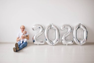 Christmas, new year and holidays concept - Proud father holding his newborn baby daughter near 2020 balloons