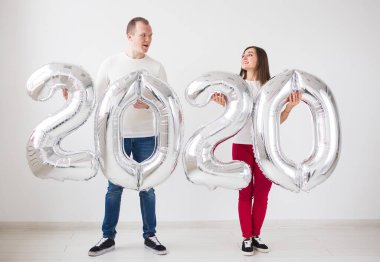 Yeni yıl, kutlama ve tatil konsepti - beyaz arka plan üzerinde yeni yıl için gümüş balonlardan yapılmış 2020 işareti ile eğlenen aşk çift