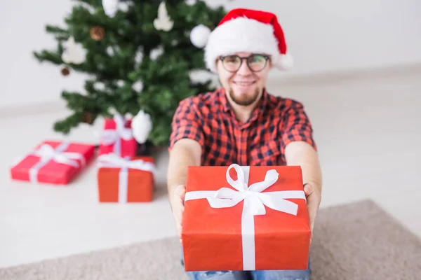 Koncepcja świąt Bożego Narodzenia i świąt - Śmieszny człowiek w kapeluszu Mikołaja trzymający prezent w domu w salonie — Zdjęcie stockowe
