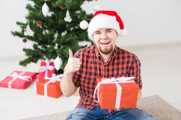 Noel et concept de vacances - Homme drôle dans le chapeau de Père Noël tenant un cadeau à la maison dans le salon — Photo