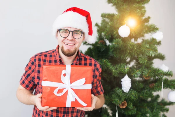 Concepto de Navidad y vacaciones - Hombre divertido en sombrero de santa celebración de un regalo en casa en la sala de estar — Foto de Stock