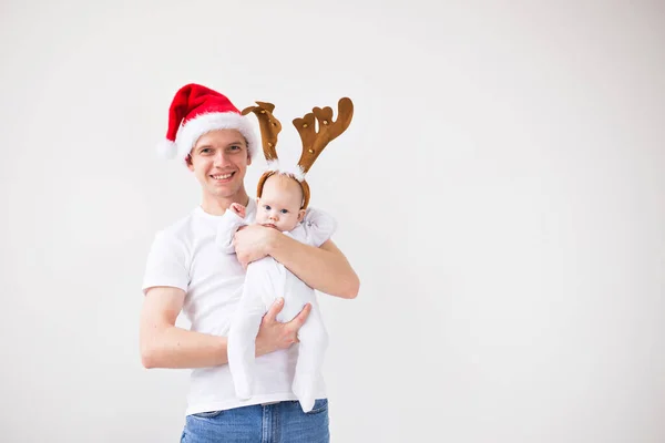 My first Christmas. Dad in santa hat holding his baby girl daughter wearing in deer horns on white background with copy space — Zdjęcie stockowe